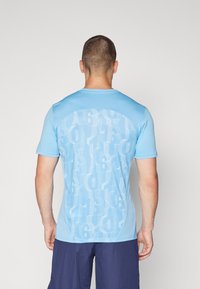 T-shirt de sport à manches courtes de couleur bleu clair, featuring un motif texturé de grands chiffres superposés au dos et un devant uni.