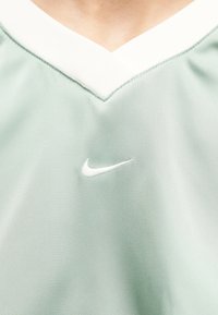 Εγγύς λήψη φωτεινού πράσινου αθλητικού μπλουζιού με λευκό V-λαιμόκοψη και λευκό λογότυπο Nike στο στήθος.