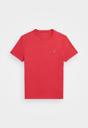 T-shirt en coton rouge avec un col rond et des manches courtes, arborant un petit logo bleu sur le côté gauche de la poitrine.