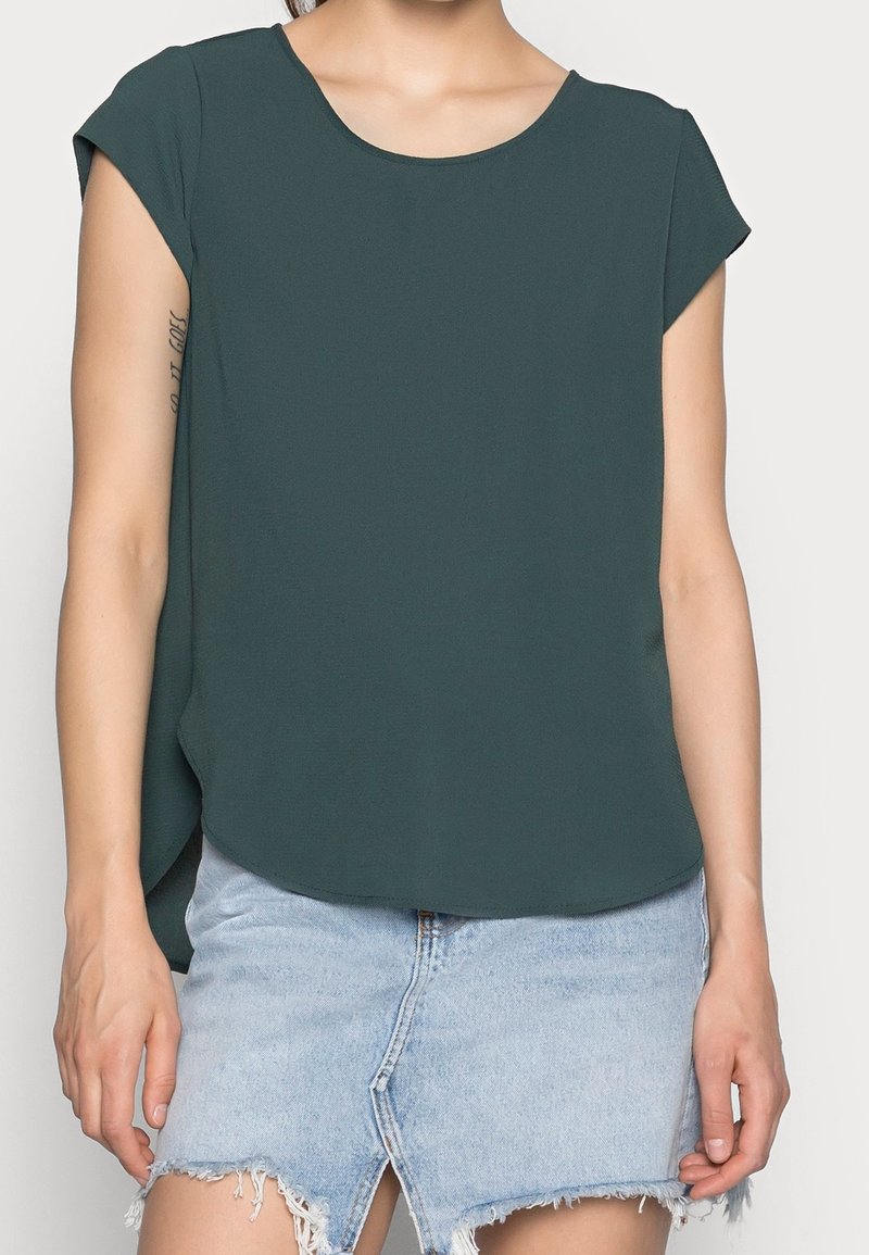 Mørkegrøn, kortærmet top med rund halsudskæring og glat tekstur, parret med en lys denim mini-nederdel med en frynset kant.