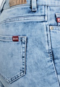 Hele sinised teksad lähivõttes, seljakotiga, kus on punane Big Star kaubamärgiga silt ja pruun Big Star nahast plaastriga vöökohal.