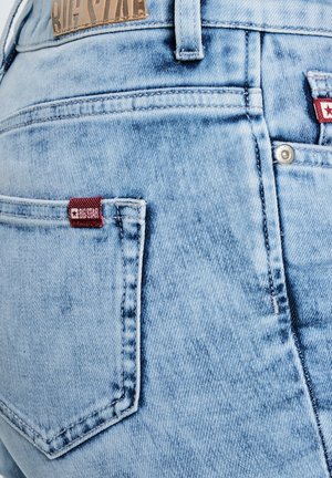 Hele sinised teksad lähivõttes, seljakotiga, kus on punane Big Star kaubamärgiga silt ja pruun Big Star nahast plaastriga vöökohal.