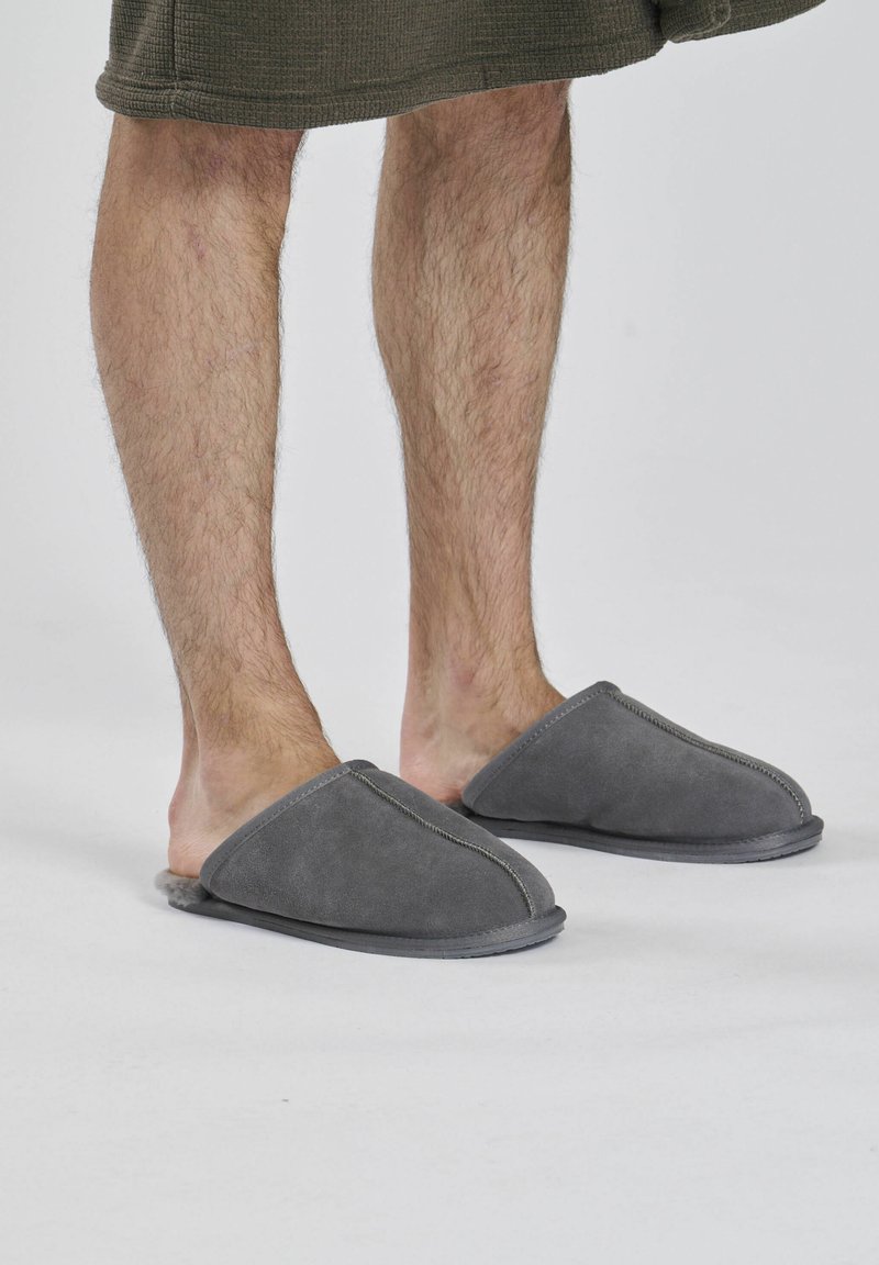 Pantofole in suede grigio con un morbido rivestimento interno, punta aperta rotonda e dettagli cuciti. Design confortevole, adatto per uso interno.