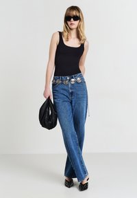 Body a maniche corte nero, jeans in denim blu a vita alta con dettagli argentati alla cintura, borsa nera, scarpe nere con punta affilata e borchie.