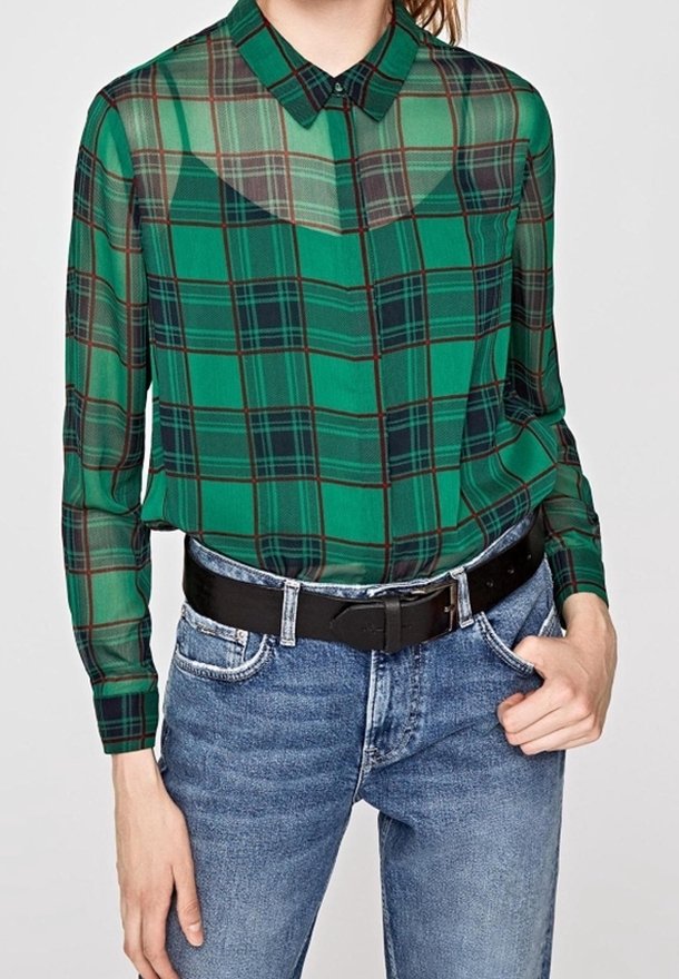Camisa de cuadros verdes con textura transparente, con mangas largas y cuello. Combinada con jeans azul de cintura alta y un cinturón negro.