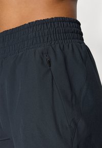 Shorts de sport en tissu navy lisse et sombre, avec une taille élastique et une poche latérale équipée d'une fermeture éclair, présentant des détails de couture discrets.
