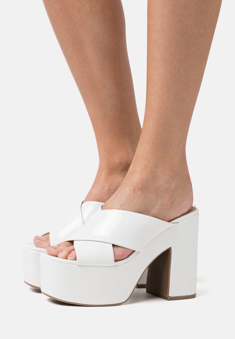 Sandali platform bianchi con una finitura lucida e liscia, design con larghe cinghie incrociate e tacco a blocco per maggiore altezza e stabilità.