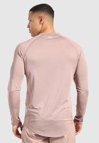 Helles rosa Longsleeve-Sportshirt mit strukturierter Oberfläche, Raglanärmel und einem Logo auf dem oberen Rücken. Glatter Stoff, taillierte Passform.