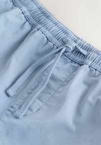 Shorts à taille élastique bleu clair avec cordon de serrage noué et surpiqûres visibles sur les poches latérales, en tissu lisse.