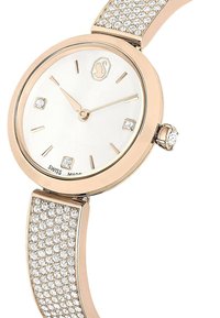 Zegarek w różowym złocie z białą tarczą, czterema znacznikami godzin przypominającymi diamenty oraz bransoletą wysadzaną kryształami. Wyprodukowano w Szwajcarii.
