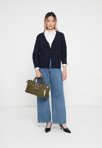 Cardigã azul-marinho em ponto de cabos, camisa branca de colarinho, jeans de perna larga, mala verde-azeitona com detalhe em estrela e sapatos de salto agudo pretos.