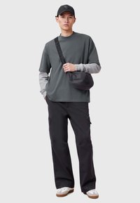 Grå kortärmad skjorta med kontrasterande grå långärmar, svarta cargobyxor och en svart axelremsväska; vita sneakers med bruna sulor.