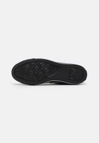 Černá gumová podrážka s texturovaným gripem, zdobená diamantovým vzorem a bílými akcentními proužky podél strany. Odolný a flexibilní materiál.