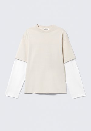 Beige short-sleeve T-shirt layered over a white long-sleeve shirt with a round neckline and "WEEKDAY" label inside collar.