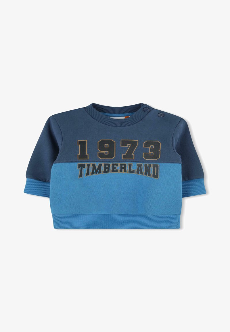 Felpa blu e blu scuro con maniche lunghe, polsini a coste, scollo rotondo e "1973 TIMBERLAND" stampato in oro. Due bottoni sulle spalle.