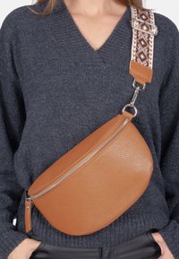 Braune Leder-Umhängetasche mit runder Form, strukturiertem Oberflächen und einem gemusterten, verstellbaren Trageriemen mit geometrischen Designs.