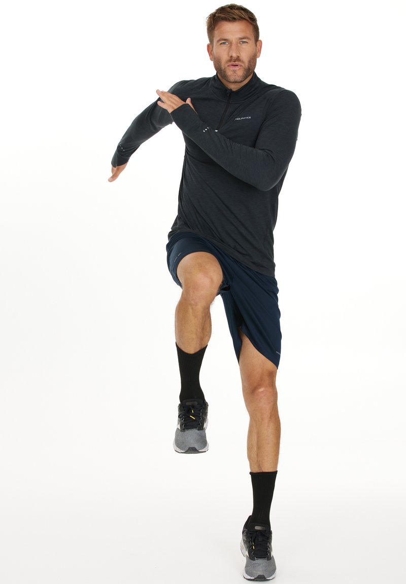 Aktive Herrenbekleidung bestehend aus einem langärmeligen, dunkelgrauen Shirt, navy Shorts, schwarzen Socken und grauen Sportschuhen. Laufpose.