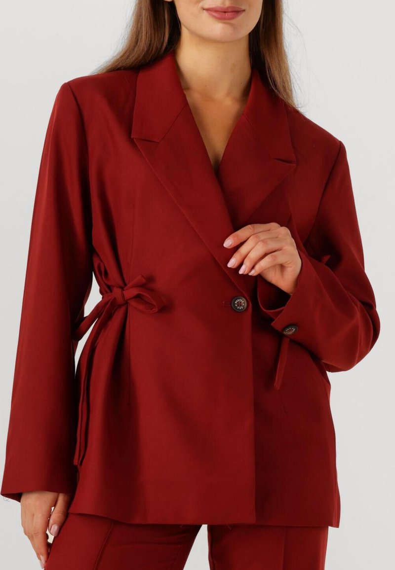Bordeaux blazer met een getailleerde pasvorm, voorzien van een notched collar, dubbele knoopsluiting en gestrikte accenten aan de zijkanten. Soepele stoftextuur.