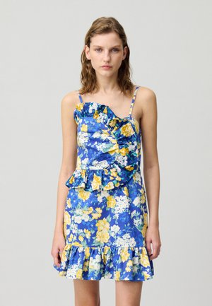 Robe mini florale bleue avec des fleurs jaunes et blanches. Encolure et ourlet volants, fines bretelles, corsage ajusté et jupe à volants.