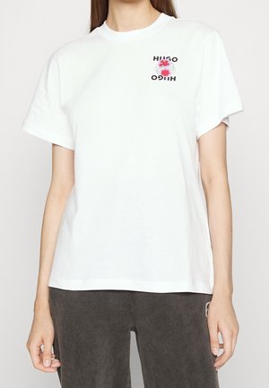 Vit bomull t-shirt med korta ärmar, rundad halsringning och en blommig logotypdesign i rött och svart på vänster sida.