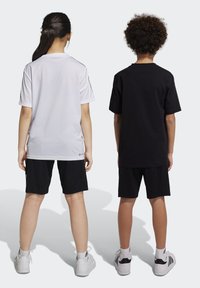 Camisetas blancas y negras de manga corta, combinadas con pantalones cortos negros. Las camisetas tienen un corte holgado; ambos llevan zapatillas deportivas blancas.