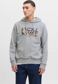 Sudadera gris con cordón, que presenta un estampado gráfico multicolor "JACK & JONES" y puños y dobladillo acanalados, llevada sobre unos jeans.