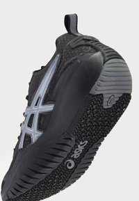 Black athletic shoe with a textured upper, light gray accents, and a rubber sole featuring a distinct tread pattern for traction.