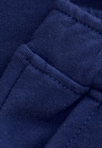 Close-up van marineblauwe ribstof met gedetailleerde stiksels en gevouwen naden.