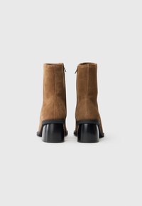 Bottes de cheville en daim marron avec un bout arrondi et un élégant talon bloc noir. Elles comportent une fermeture éclair à l'arrière pour un enfilage facile.