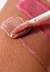 Glossy pink and rose gold liquid lipsticks swatched on skin with applicator wand applying rose gold shade.