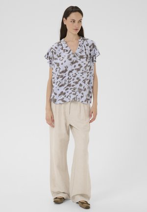 Lichte, kortarmige blouse in lichtblauw met een bruin abstract patroon, met een V-hals en een ontspannen pasvorm. Gepaarde met beige wijde broekspijpen.