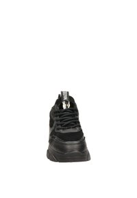 Zapatilla negra con una combinación de materiales de cuero y ante, que presenta una suela gruesa, puntera redondeada y un diseño de cordones negros. Incluye una tira de agarre.