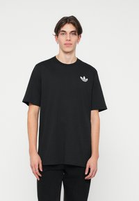 Černé bavlněné tričko s krátkými rukávy a kulatým výstřihem, s bílým logem trefoil Adidas na levé straně hrudi.