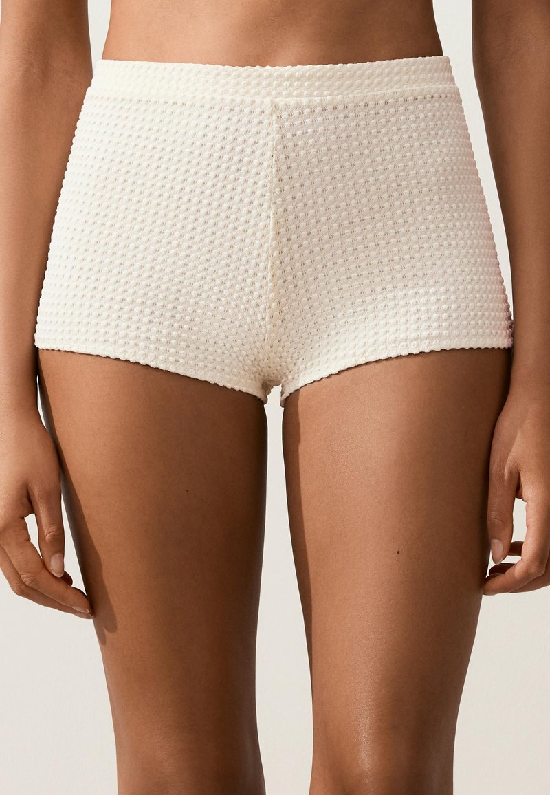 Vue de la taille jusqu'au milieu de la cuisse d'une personne portant un short texturé couleur crème à taille haute avec un motif en maille gaufrée.