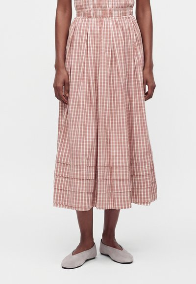 Woman wearing a pink and white checkered midi skirt with pleats at the hem and light gray flat shoes, standing on a plain background.