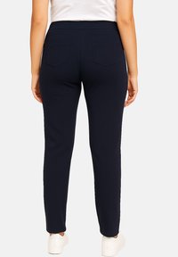 Navy blue stretchy pants with a smooth texture, featuring a high waistband and two back pockets. Styled with white sneakers.