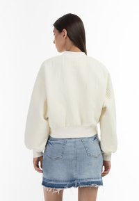 Witte textuur bomberjack met een aansluitende tailleband, elastische manchetten en een ronde kraag, gedragen over een denim minirok.