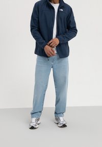 Marinblå fleecejacka med ståkrage och frontdragkedja, ihopparad med ljusblå löst sittande jeans och silverfärgade löparskor.