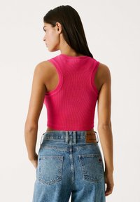 Fitted roze geribde tanktop met een ronde halslijn en mouwloos ontwerp, gecombineerd met high-waisted blauwe denim jeans met achterzakken.