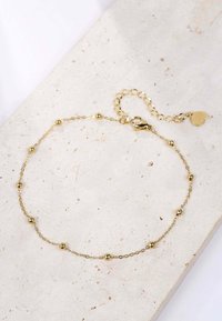Pulsera de cadena de oro que presenta pequeñas cuentas esféricas, un cierre de langosta y una cadena ajustable con un charm en forma de corazón.