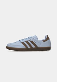 Ανοιχτό γαλάζιο αθλητικό παπούτσι Adidas Samba με τρεις καφέ ρίγες, καφέ σόλα και κλείσιμο με κορδόνια, εμφανίζεται σε πλάγια όψη.