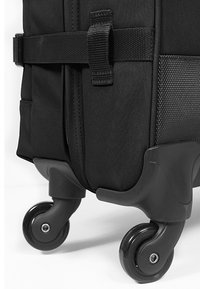 Black suitcase with textured fabric, features a thick strap, and four swivel wheels. Visible stitching and reinforced corners.