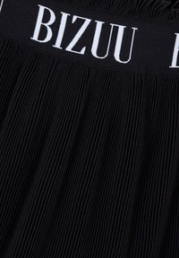 Zwarte plooienrok met een brede elastische tailleband met daarop de witte tekst "BIZUU". De plooien lopen verticaal door de stof.