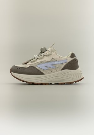 Beige og brun sneaker med tyk sål, paneler af mesh og ruskind, lynsnøresystem, blå "SHADOW"-logo på siden, mod ensfarvet baggrund.