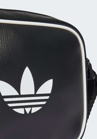 Čierna syntetická kožená taška so bielym lemovaním, veľkým bielym logom s tromi listami a pruhmi a štruktúrovaným povrchom.