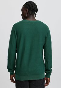 Grüner strukturierter Strickpullover mit langen Ärmeln und gerippten Bündchen, mit einem geraden Saum und seitlichen Schlitzen. Die Rückansicht zeigt die Nahtdetails.