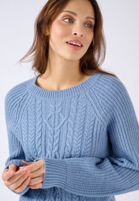 Lichtblauwe kabelgebreide trui met een ronde hals en geribbelde boorden. Heeft gestructureerde patronen aan de voorkant en mouwen.