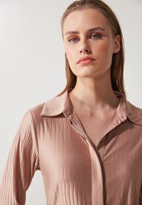 Light pink, ribbed satin shirt with a pointed collar and buttons, featuring a smooth texture and a tailored fit.