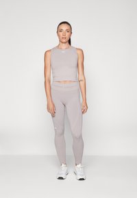 Lys grå sport crop top og matchende leggings laget av elastisk materiale, med en tettsittende design og subtil branding på kanten.