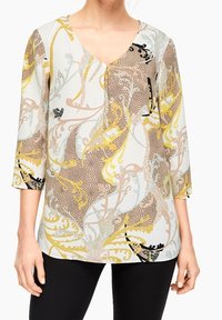 Blusa a fantasia con scollo a V, maniche 3/4 e motivi floreali in giallo, nero e colori pastello su fondo chiaro.